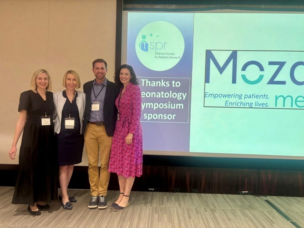 Four individuals standing in front of a large screen at a conference. The screen displays the Midwest Society for Pediatric Research logo and text reading 'Thanks to Neonatology Symposium sponsor' alongside the Mozarc Medical logo with the tagline 'Empowering patients. Enriching lives