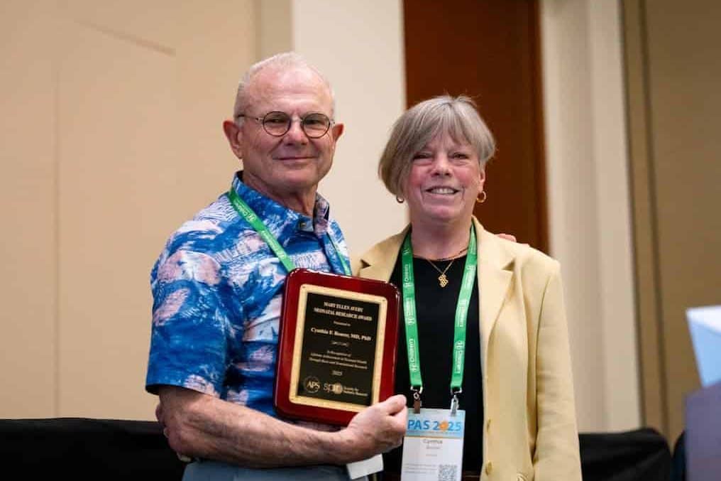 Two individuals stand together at the Pediatric Academic Societies 2025 Meeting, one holding an award plaque.