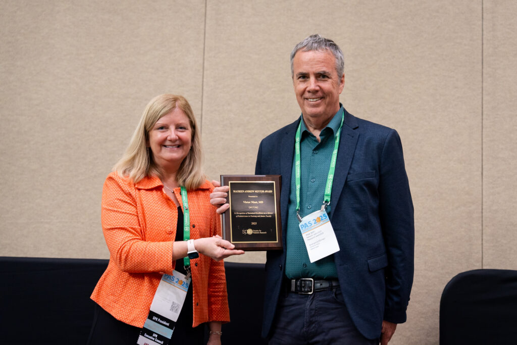 Two people standing indoors holding a plaque together, with conference badges visible.