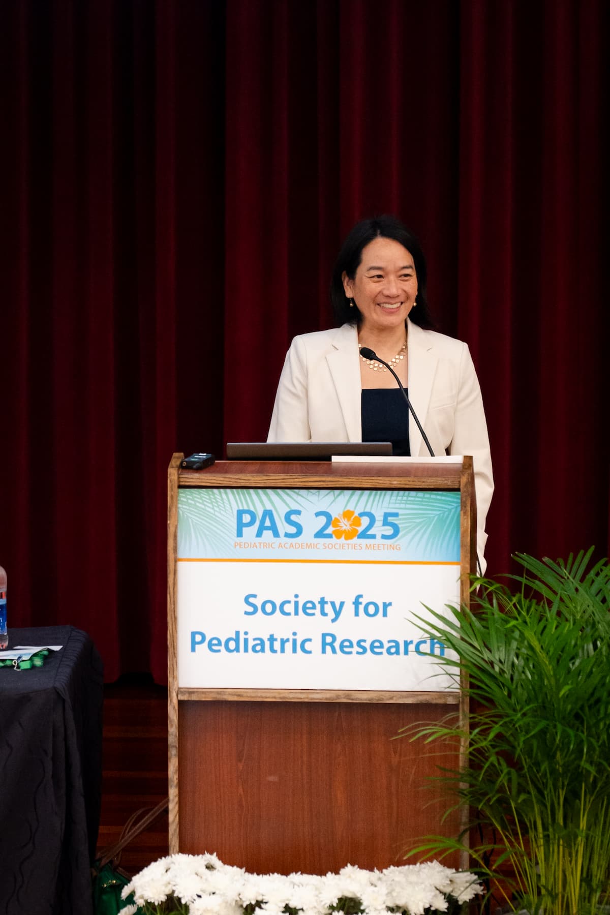 Person standing at a podium with a sign reading “PAS 2025 Society for Pediatric Research” in front of a red curtain.