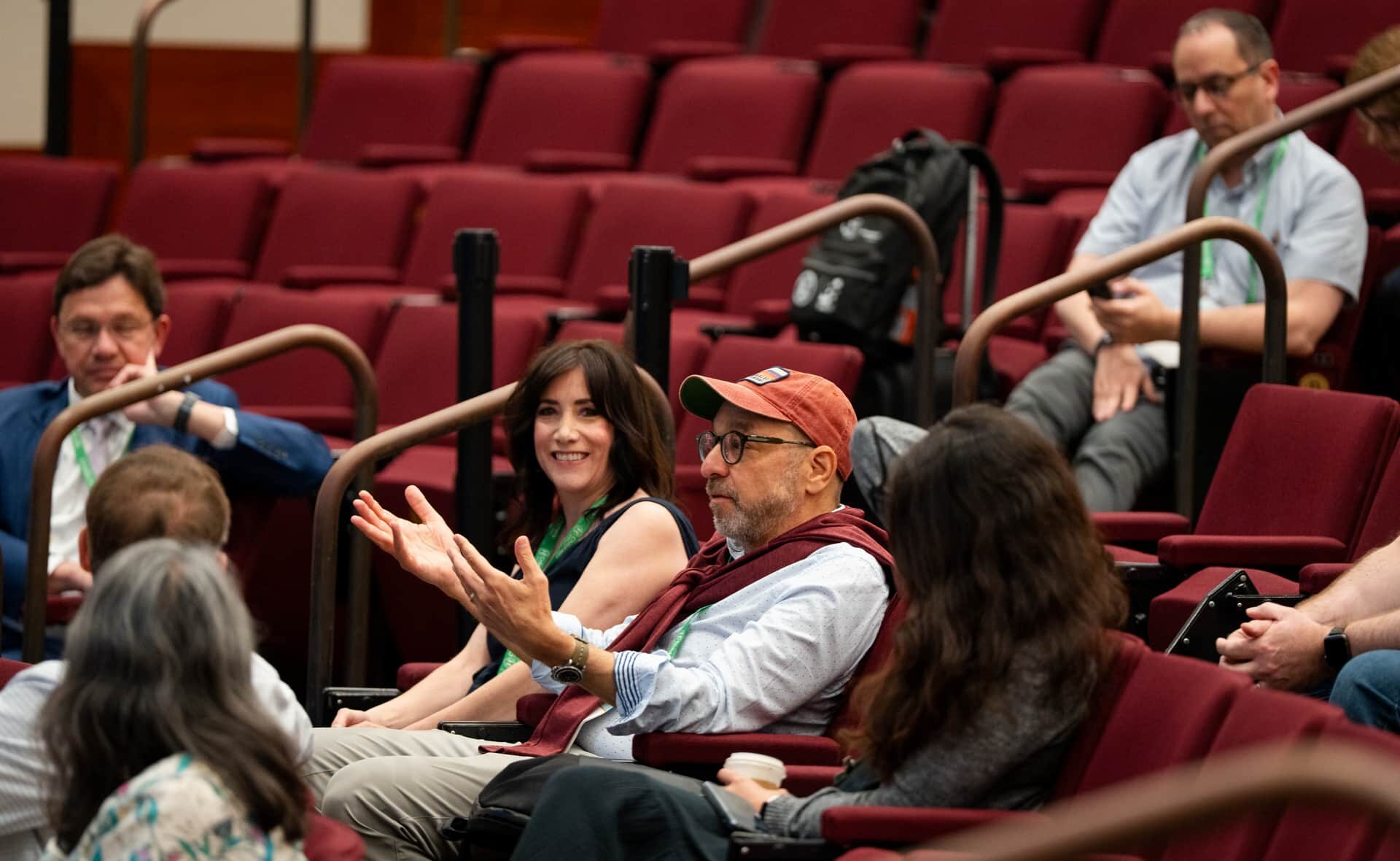 Audience members seated in a lecture hall, one person gesturing during a discussion