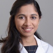 Person in a white lab coat standing against a plain gray background.