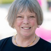 Person with short gray hair, wearing a black top and beaded necklace, smiling at the camera.