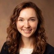 Person with curly hair smiling at the camera against a plain brown background.