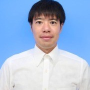 Person wearing a white collared shirt, facing the camera with a neutral expression against a blue background.