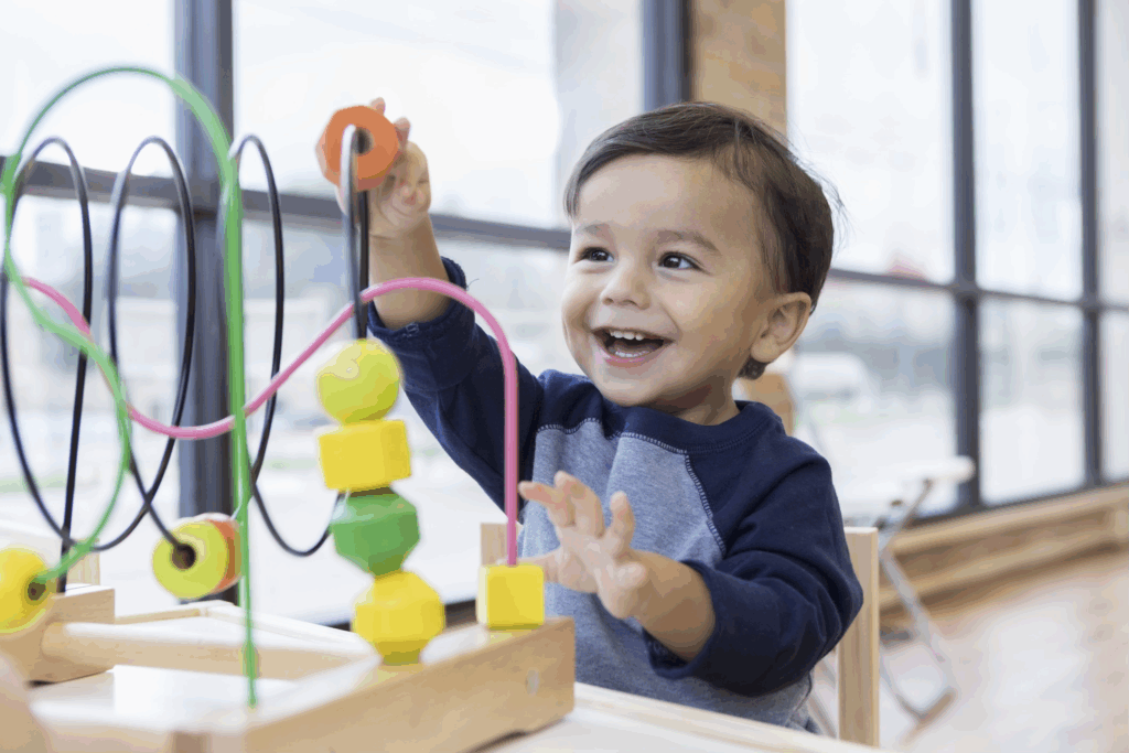 A young child plays with a colorful bead maze toy in a bright indoor setting.