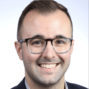 A person in a suit and glasses smiles against a light blue and white gradient background.