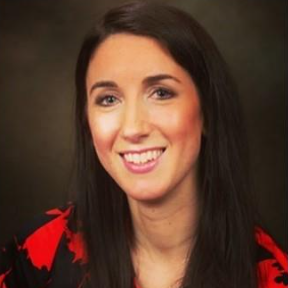 Person with long dark hair wearing a red and black patterned top, smiling in front of a dark gradient background with lighting that highlights the face.