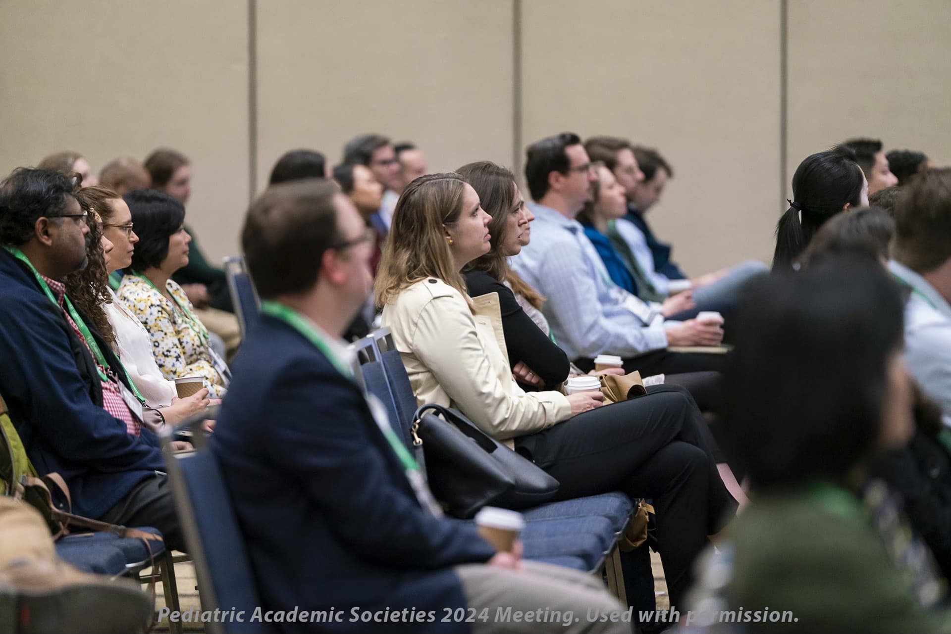 People seated in rows at a conference, facing forward with coffee cups and name badges. Text reads: "Pediatric Academic Societies 2024 Meeting. Used with permission."