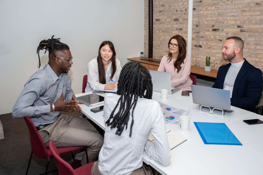 team of professionals, five multi ethnic business people negotiating in boardroom, discuss project, consider contract terms and conditions, solve business. Formal meeting event concept